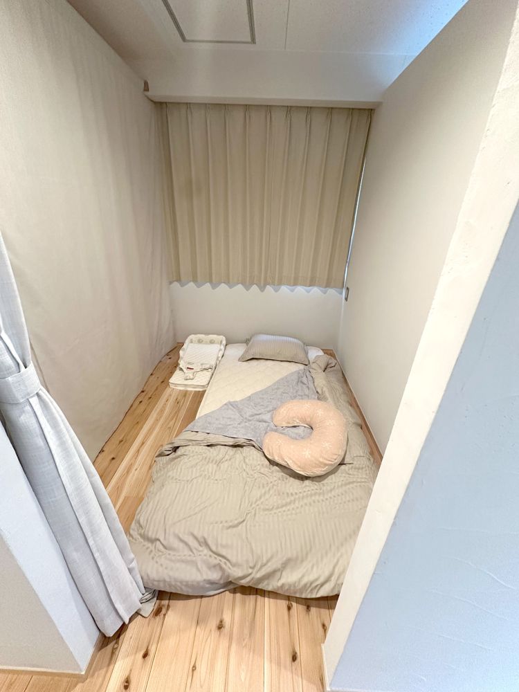 2畳くらいの部屋に、お母さんと赤ちゃん用の布団が敷かれている。床は無垢材で、部屋の入口はカーテンで仕切られている。